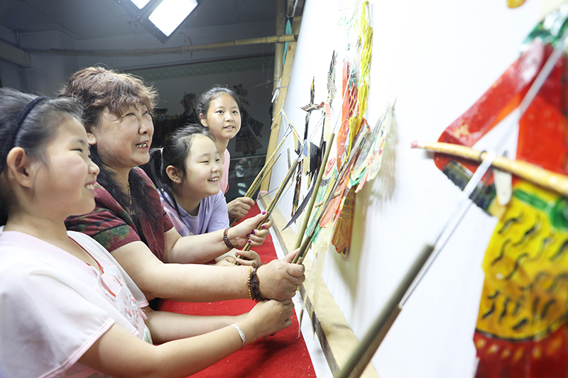 皮影藝人指導(dǎo)小朋友表演皮影戲。